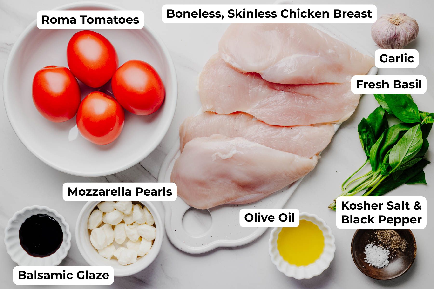 Labeled ingredients for bruschetta chicken, including chicken breasts, Roma tomatoes, fresh basil, garlic, mozzarella pearls, olive oil, balsamic glaze, kosher salt, and black pepper.