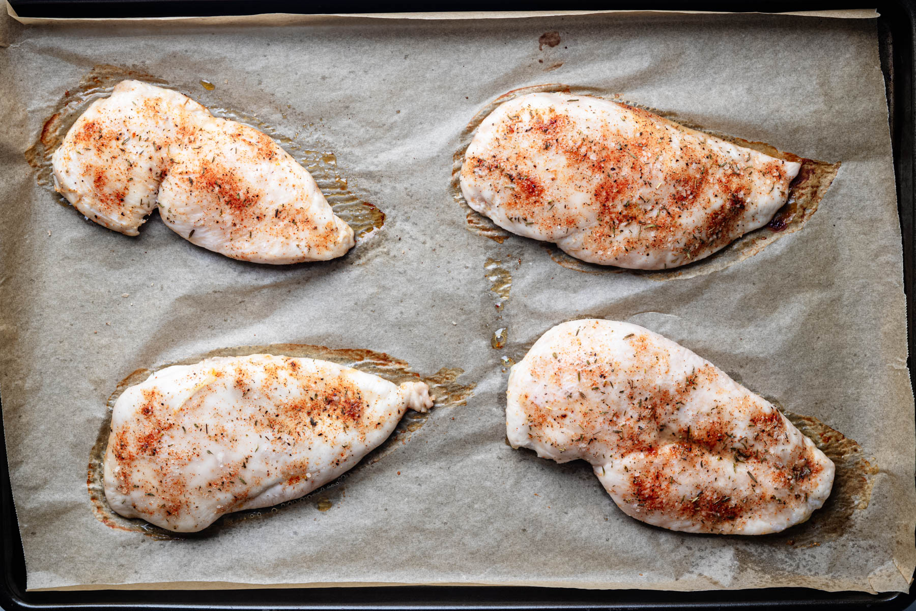 Baked garlic herb chicken breast cutlets on a parchment-lined baking sheet.
