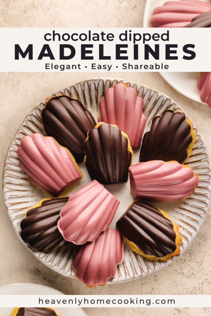 A plate of chocolate-dipped madeleines coated in dark chocolate and pink chocolate, arranged in a circular pattern on a ceramic serving plate with additional madeleines in the background. This vertical Pinterest pin features a homemade chocolate dipped madeleines recipe from Heavenly Home Cooking.