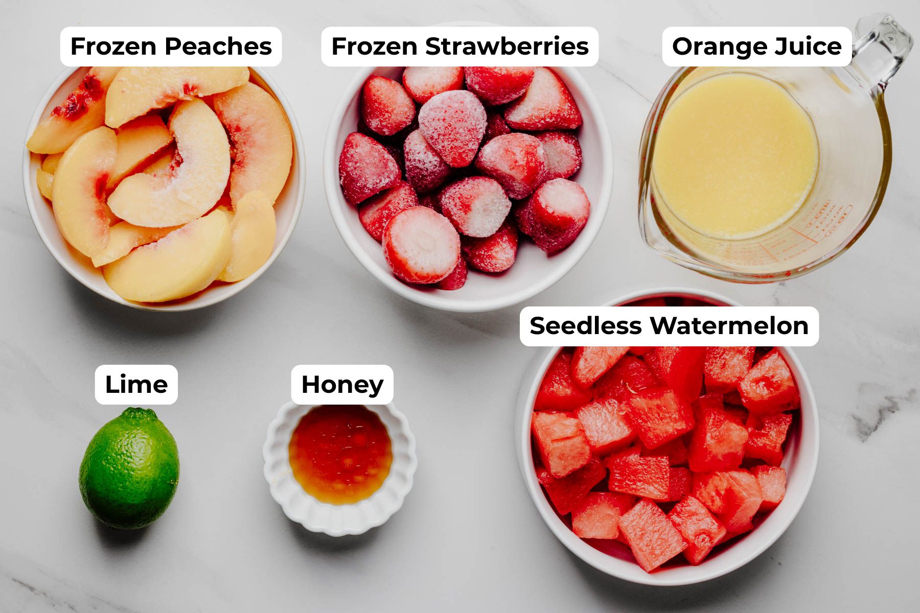 Overhead view of frozen peaches, frozen strawberries, seedless watermelon, orange juice, lime, and honey labeled as the ingredients for cold fruit soup.
