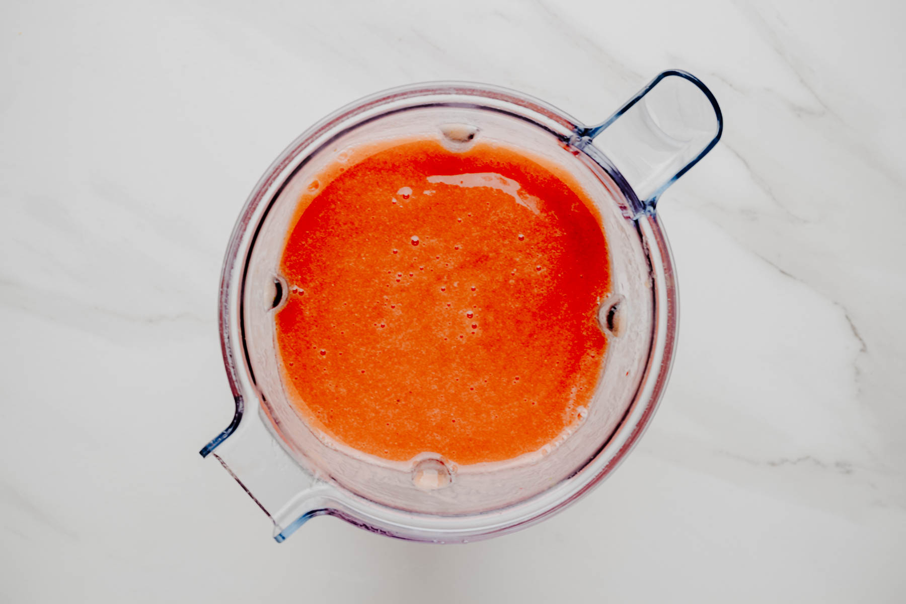 Overhead view of smooth, coral-colored cold fruit soup blended in a blender pitcher.
