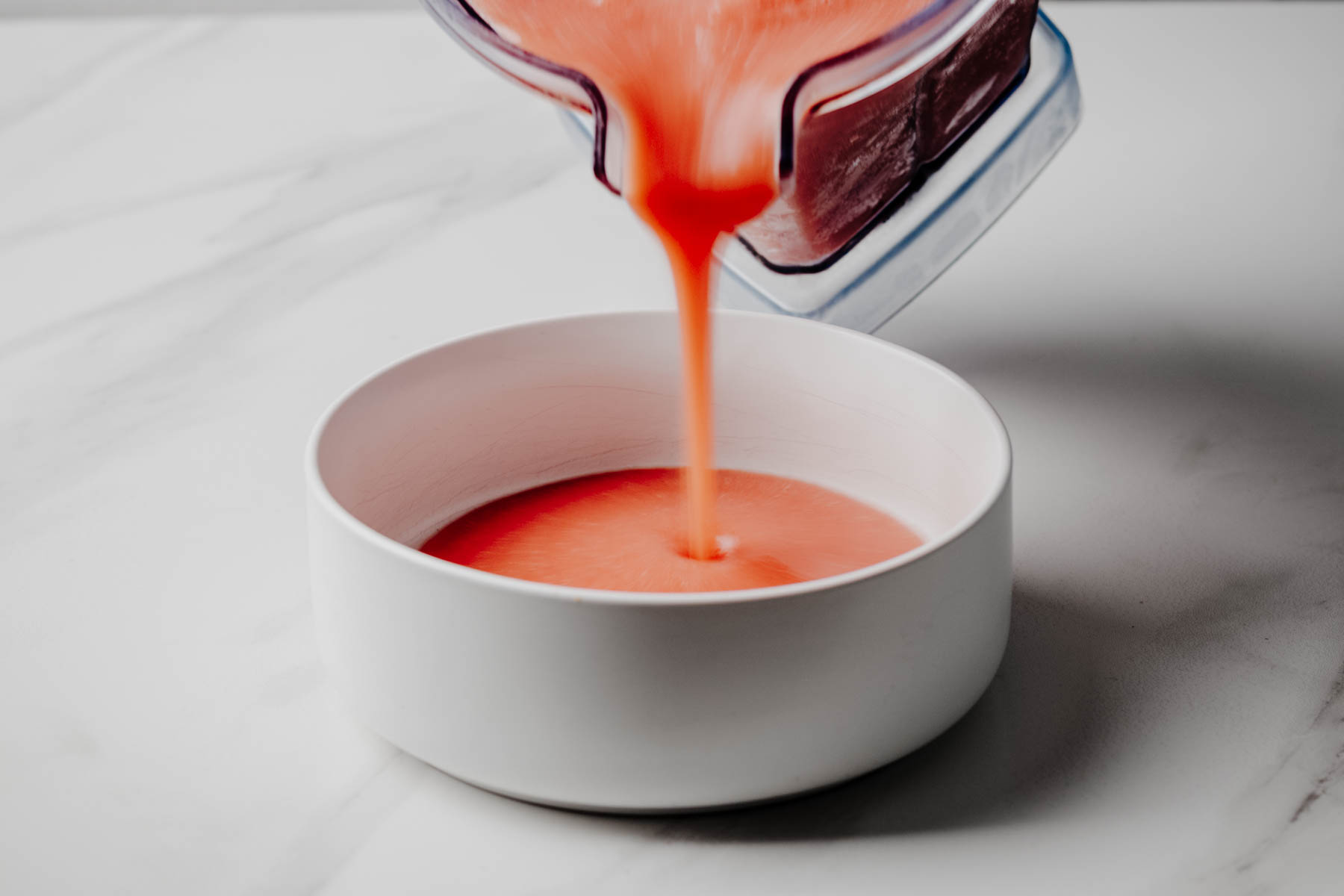 Smooth cold fruit soup being poured from a blender into a white bowl.