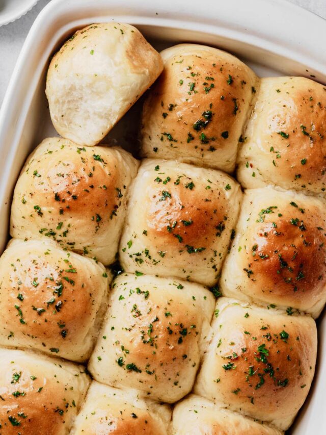 A baking dish filled with homemade garlic dinner rolls brushed with garlic butter and sprinkled with fresh parsley.