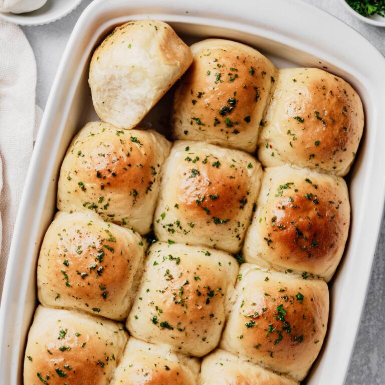 A baking dish filled with homemade garlic dinner rolls brushed with garlic butter and sprinkled with fresh parsley.