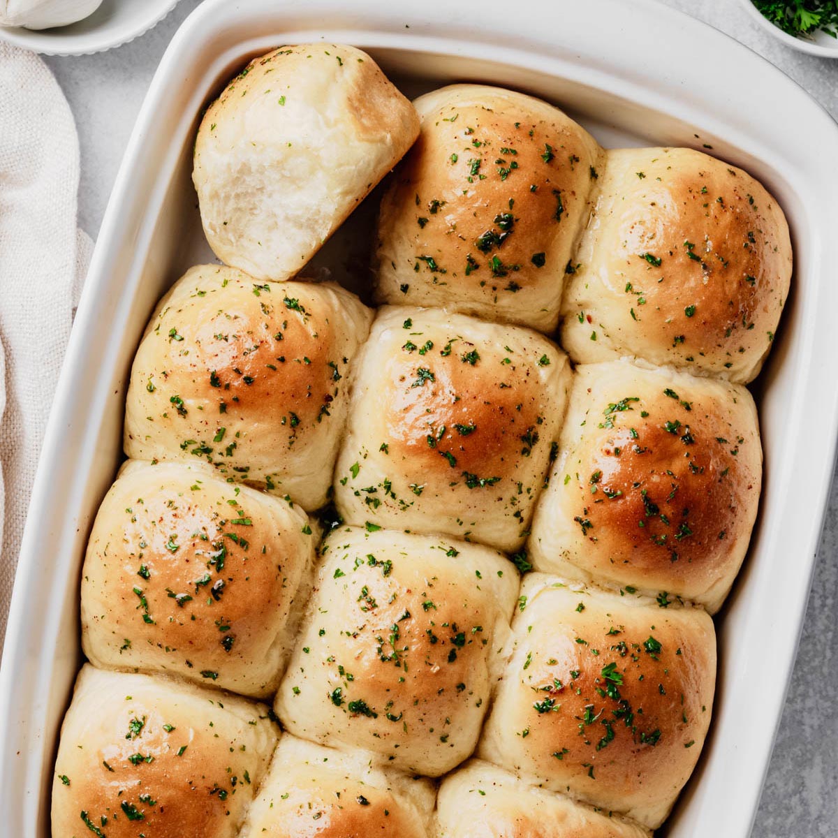 A baking dish filled with homemade garlic dinner rolls brushed with garlic butter and sprinkled with fresh parsley.