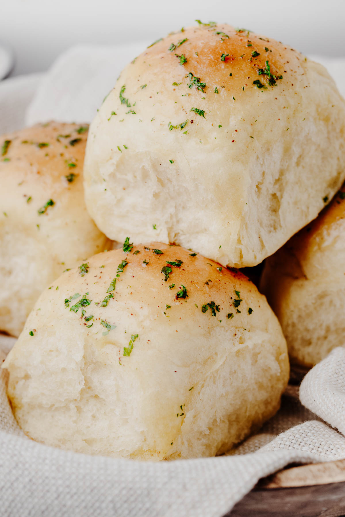 Soft homemade garlic dinner rolls stacked on a linen towel, brushed with garlic butter and sprinkled with fresh parsley.