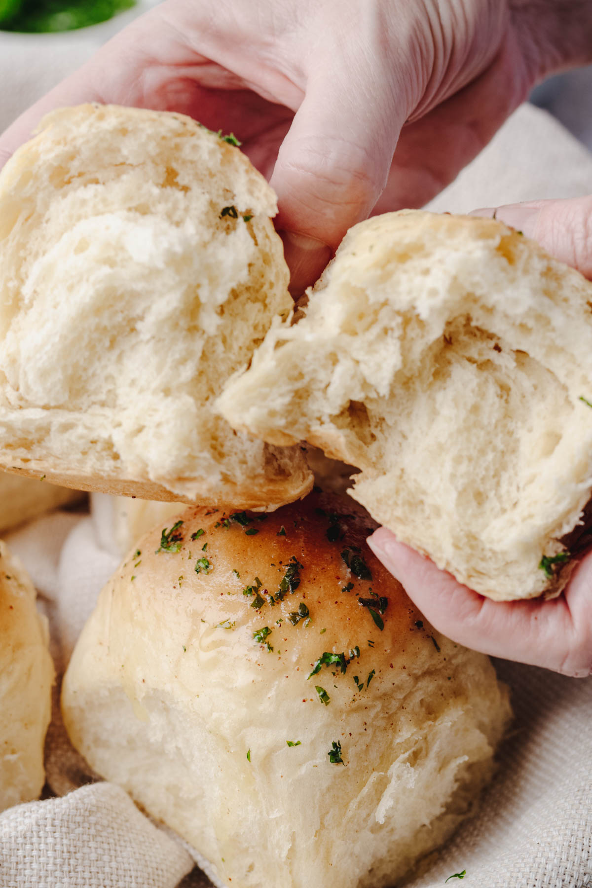 Hands pulling apart a warm homemade garlic dinner roll to reveal its soft, fluffy interior.