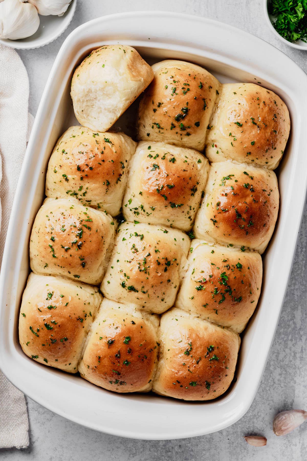 Overhead view of homemade garlic dinner rolls baked until golden brown in a white baking dish with garlic butter and parsley.