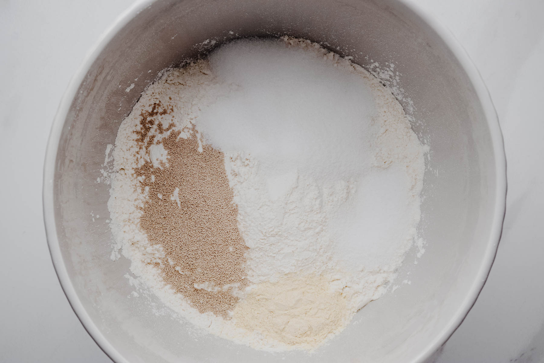 Overhead view of the dry ingredients for garlic dinner rolls in a large mixing bowl.