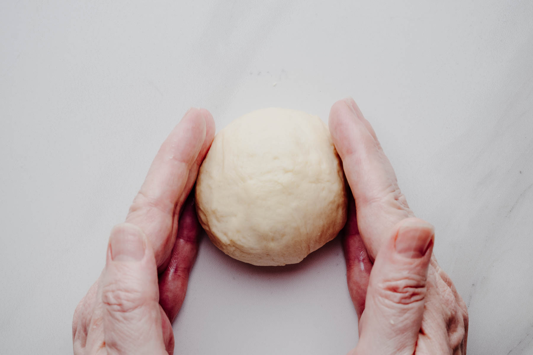 Smooth ball of garlic dinner roll dough after shaping.