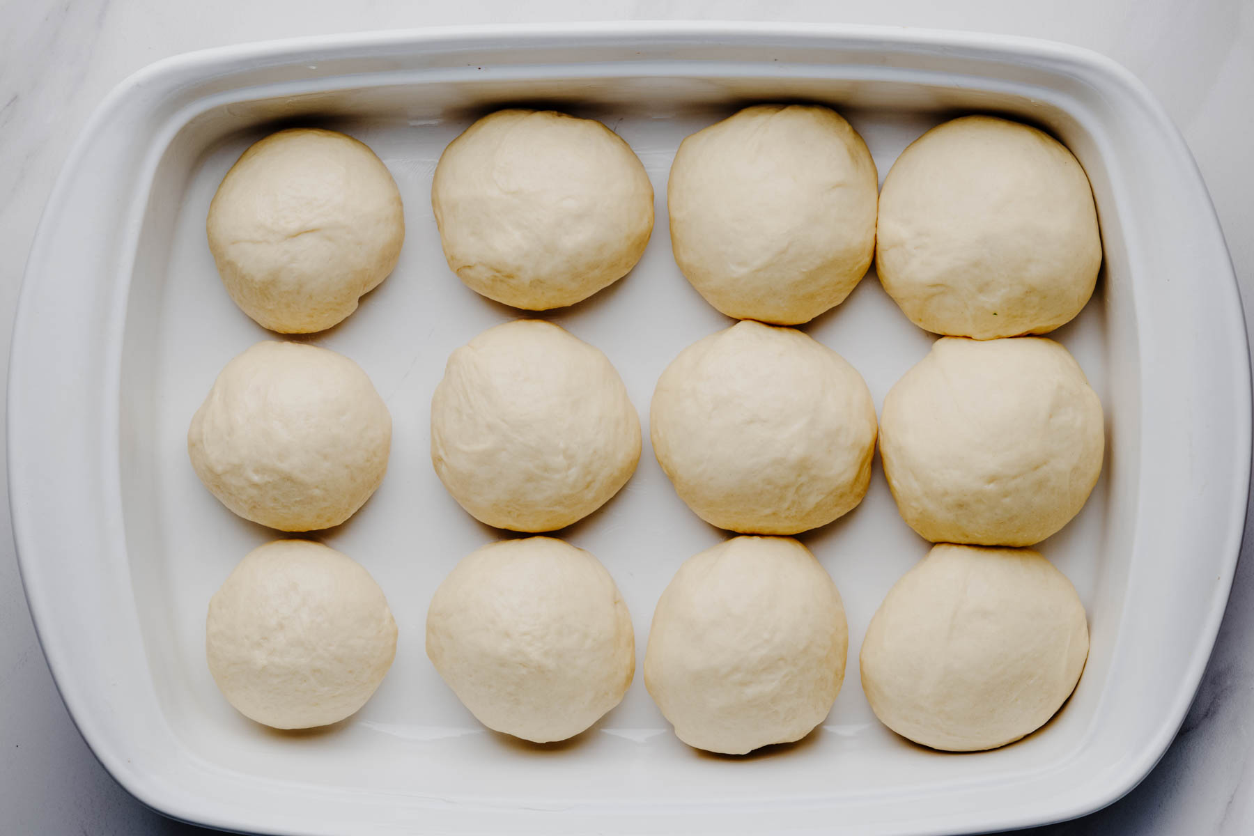 Shaped garlic dinner roll dough arranged in a baking dish before the second rise.