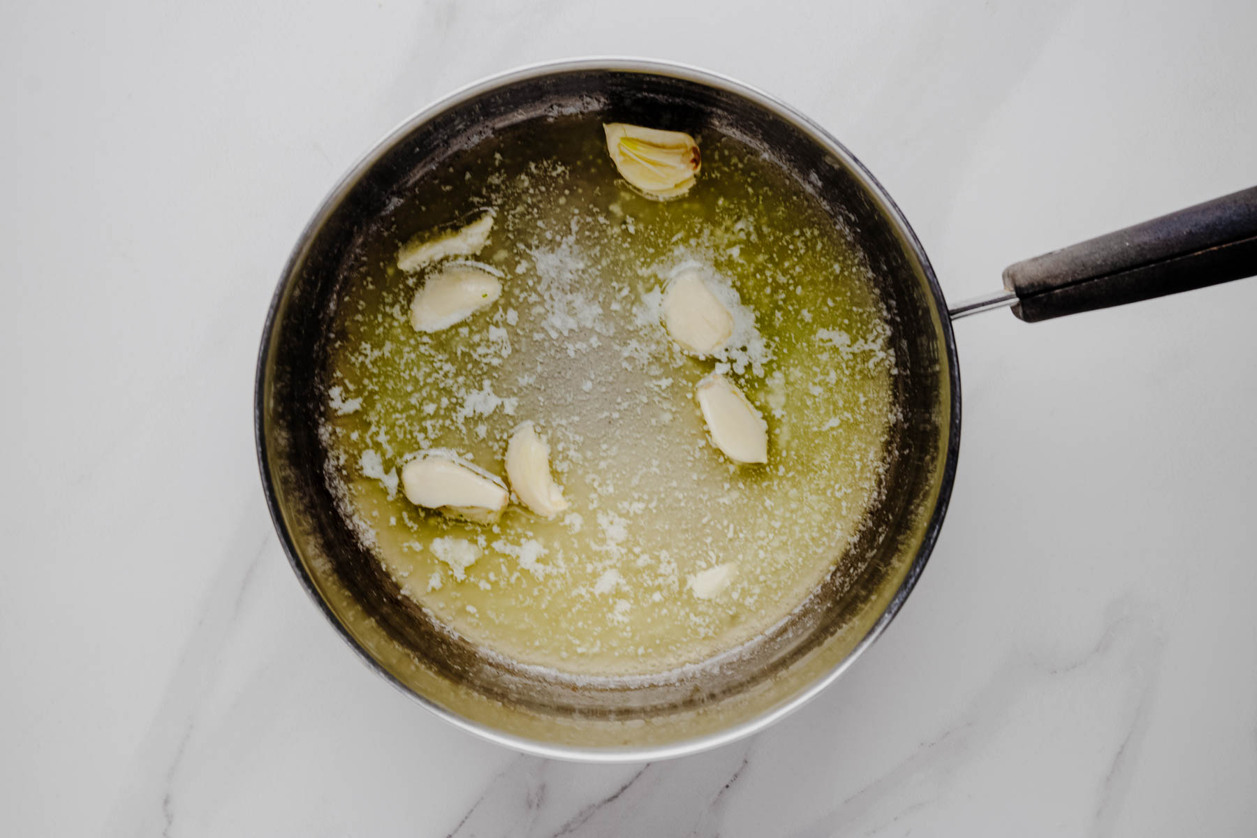 Garlic cloves gently infusing melted butter in a saucepan.