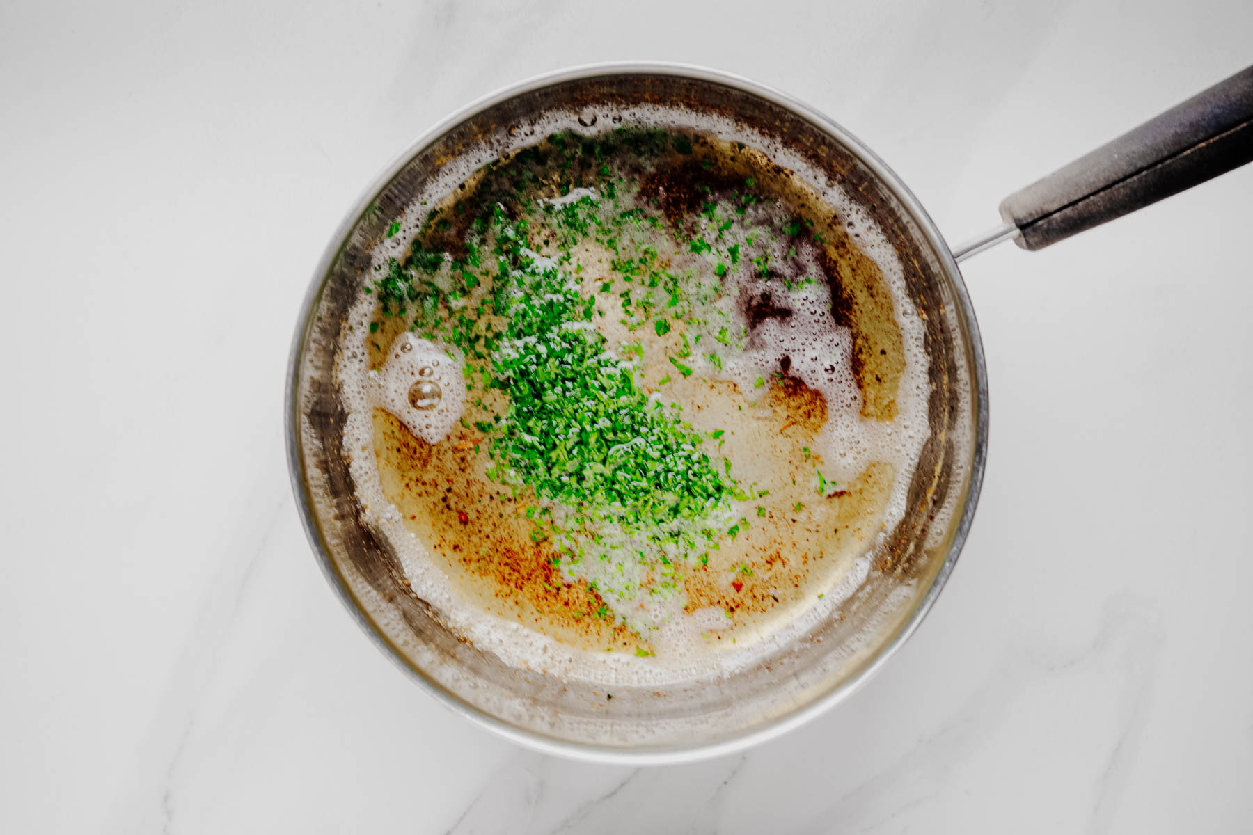 Garlic butter with chopped parsley and seasonings in a saucepan.