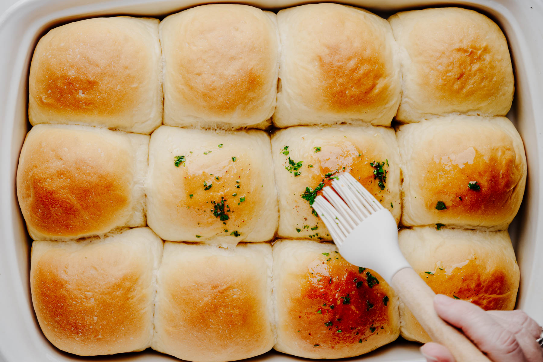 Freshly baked garlic dinner rolls being brushed with homemade garlic butter.