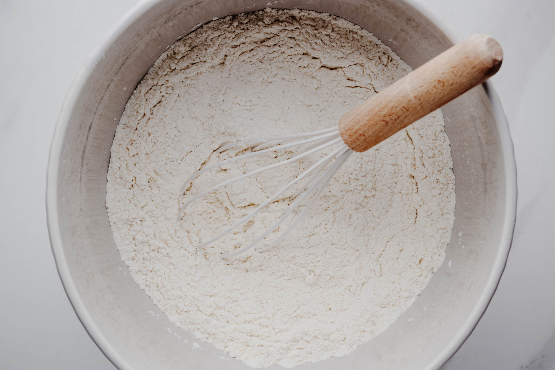 Overhead view of the dry ingredients for garlic dinner rolls whisked together in a large mixing bowl.
