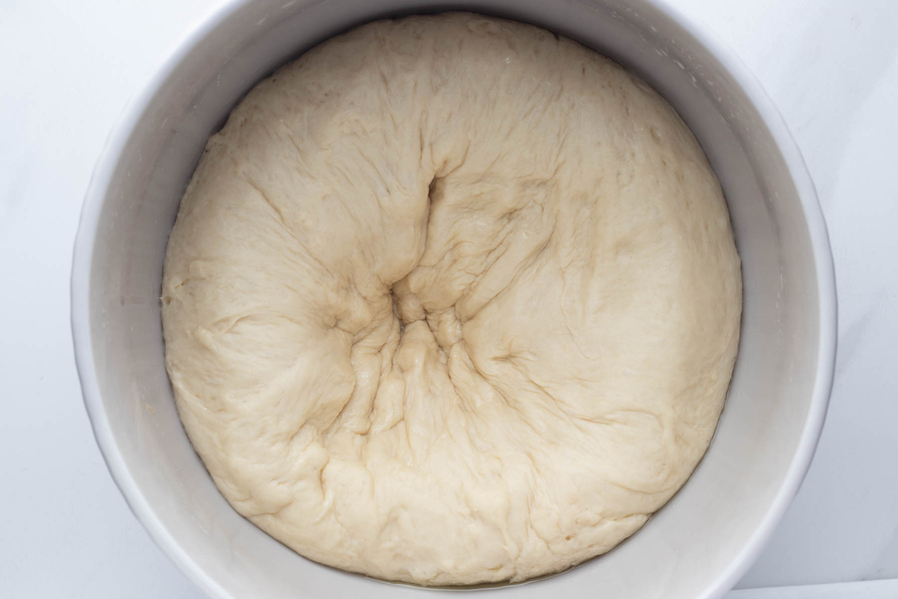 Risen garlic dinner roll dough being punched down in the mixing bowl after the first rise.