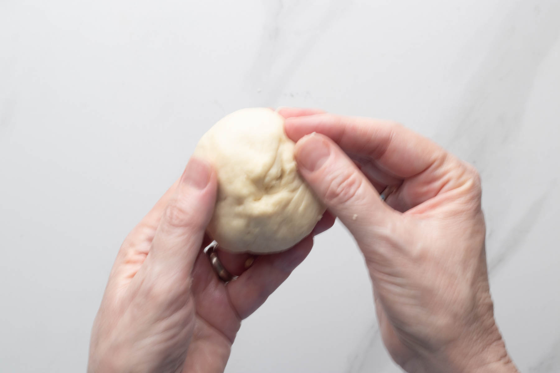 Hands shaping a portion of garlic dinner roll dough into a smooth ball.