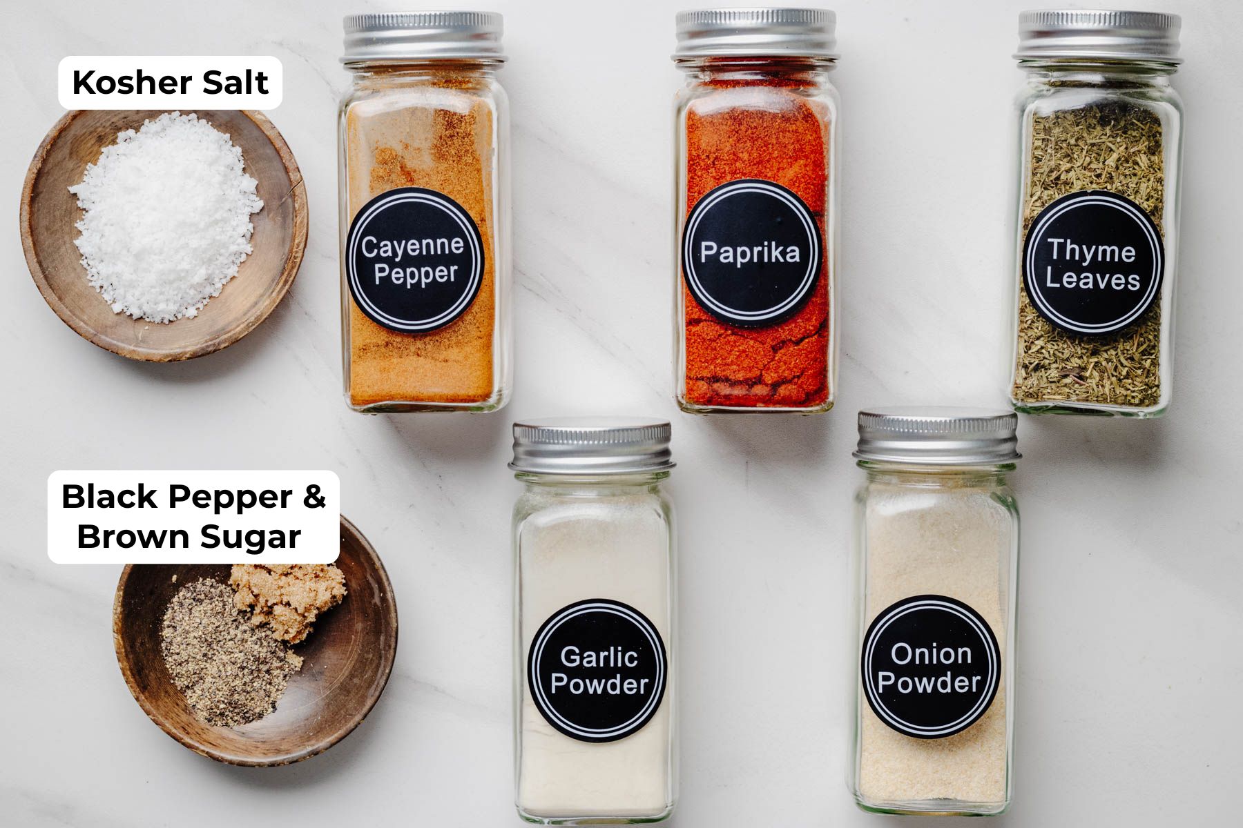 Kosher salt, cayenne pepper, paprika, dried thyme, black pepper, brown sugar, garlic powder, and onion powder arranged for making Garlic Herb Dry Brine.