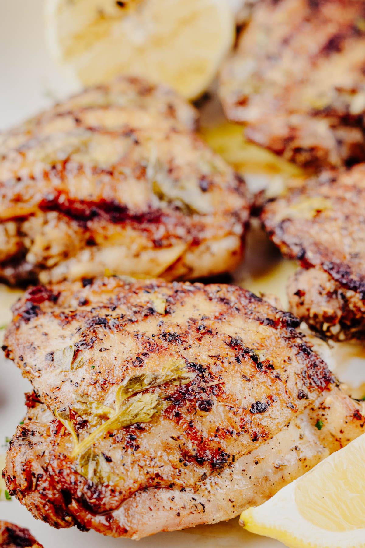 Close-up of grilled lemon herb chicken thighs on a serving platter with charred lemon and fresh parsley.