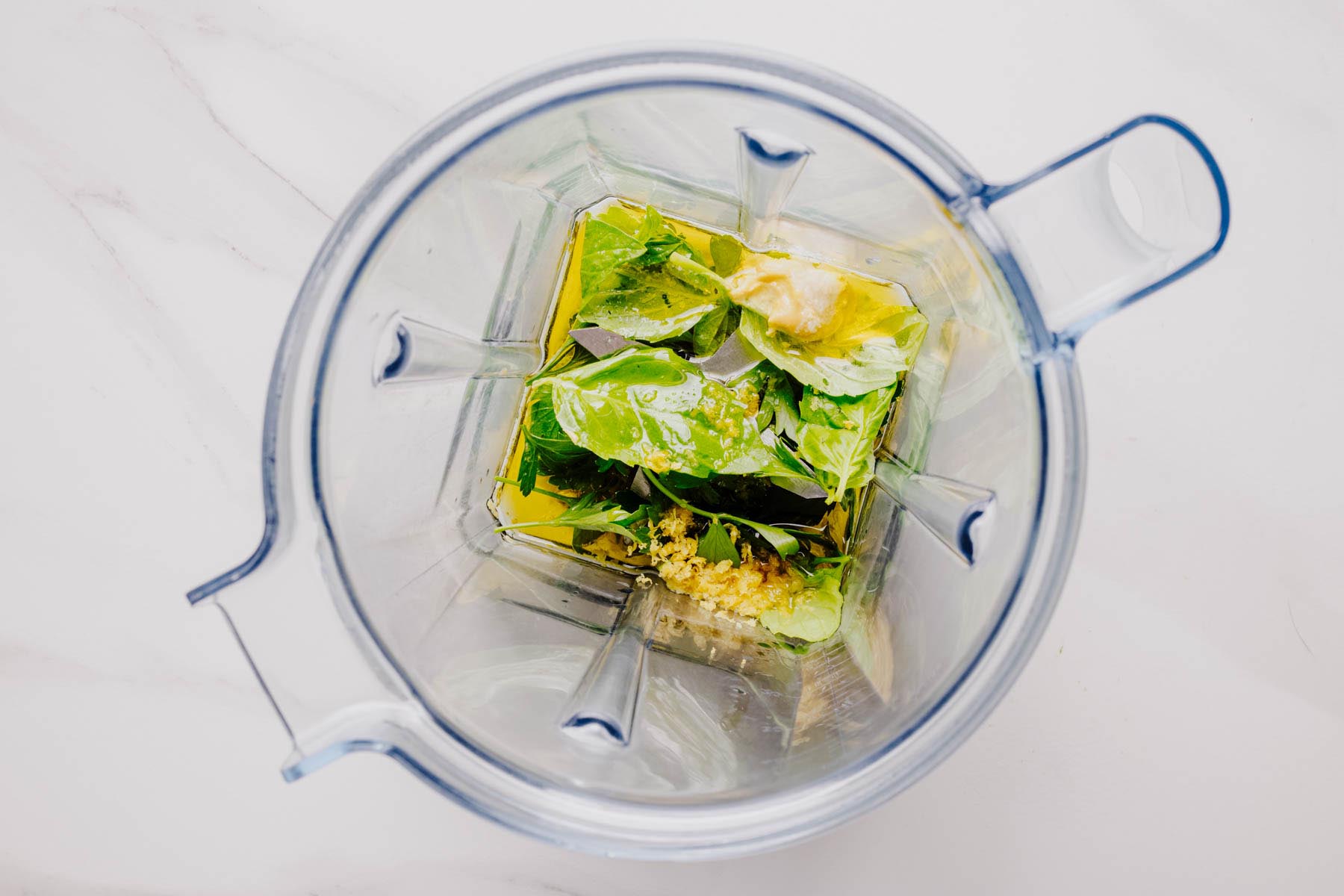 Fresh basil, parsley, garlic, lemon juice, olive oil, and seasonings in a blender before blending into a sauce.