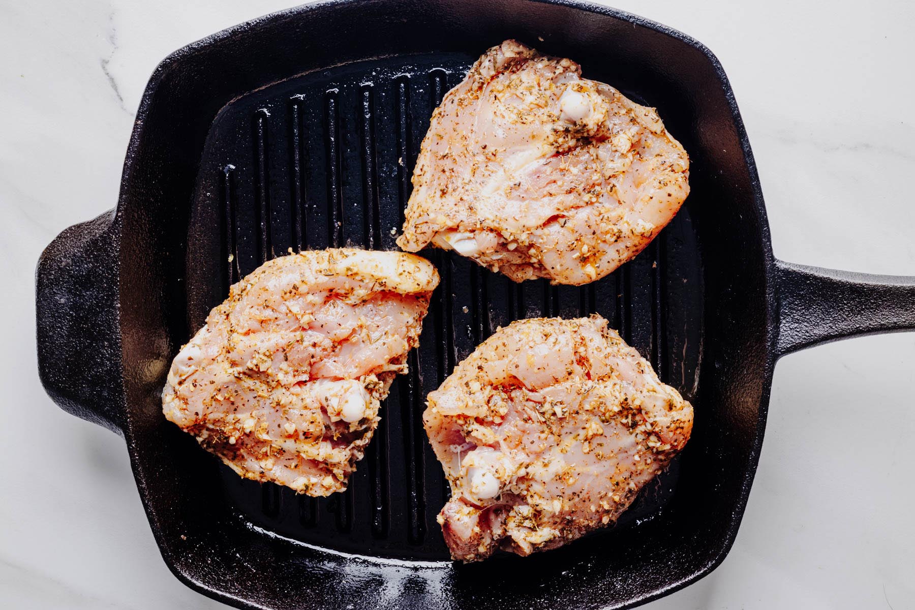 Seasoned chicken thighs arranged skin-side down on a hot grill pan before cooking.
