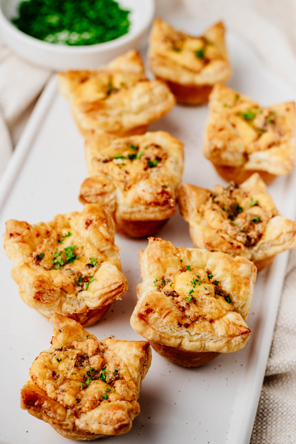 Golden sausage puff pastry cups filled with creamy Italian sausage and cheddar and arranged on a rectangular serving platter.