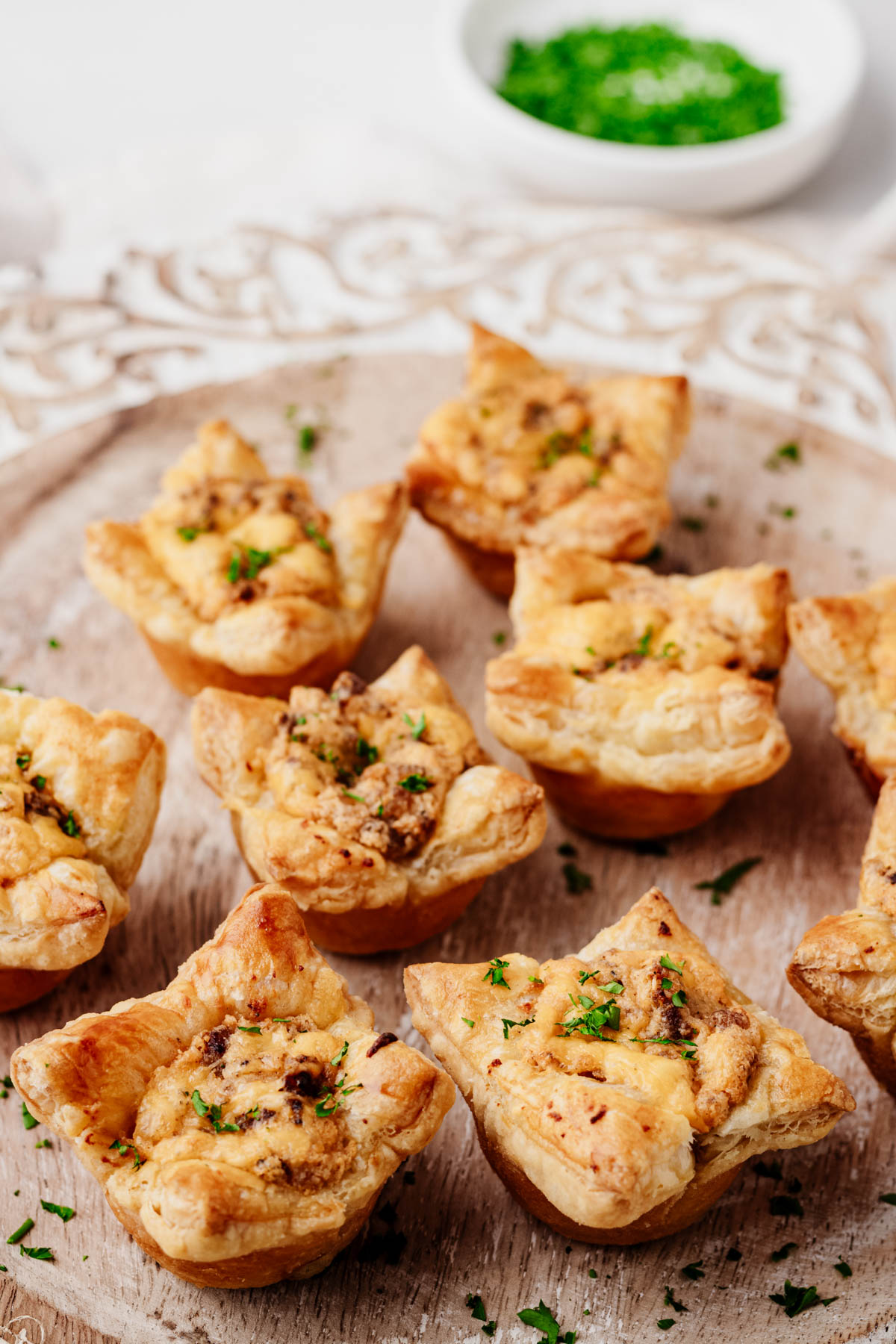 Sausage puff pastry cups garnished with parsley and arranged on a round wooden serving board.