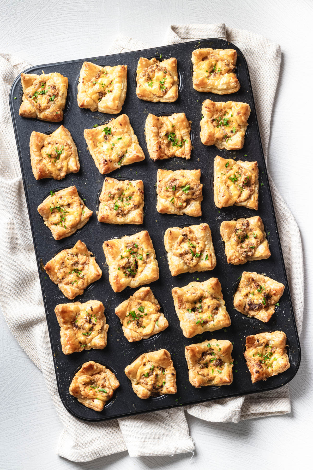 Overhead view of 24 golden sausage puff pastry cups garnished with parsley in a mini muffin pan.