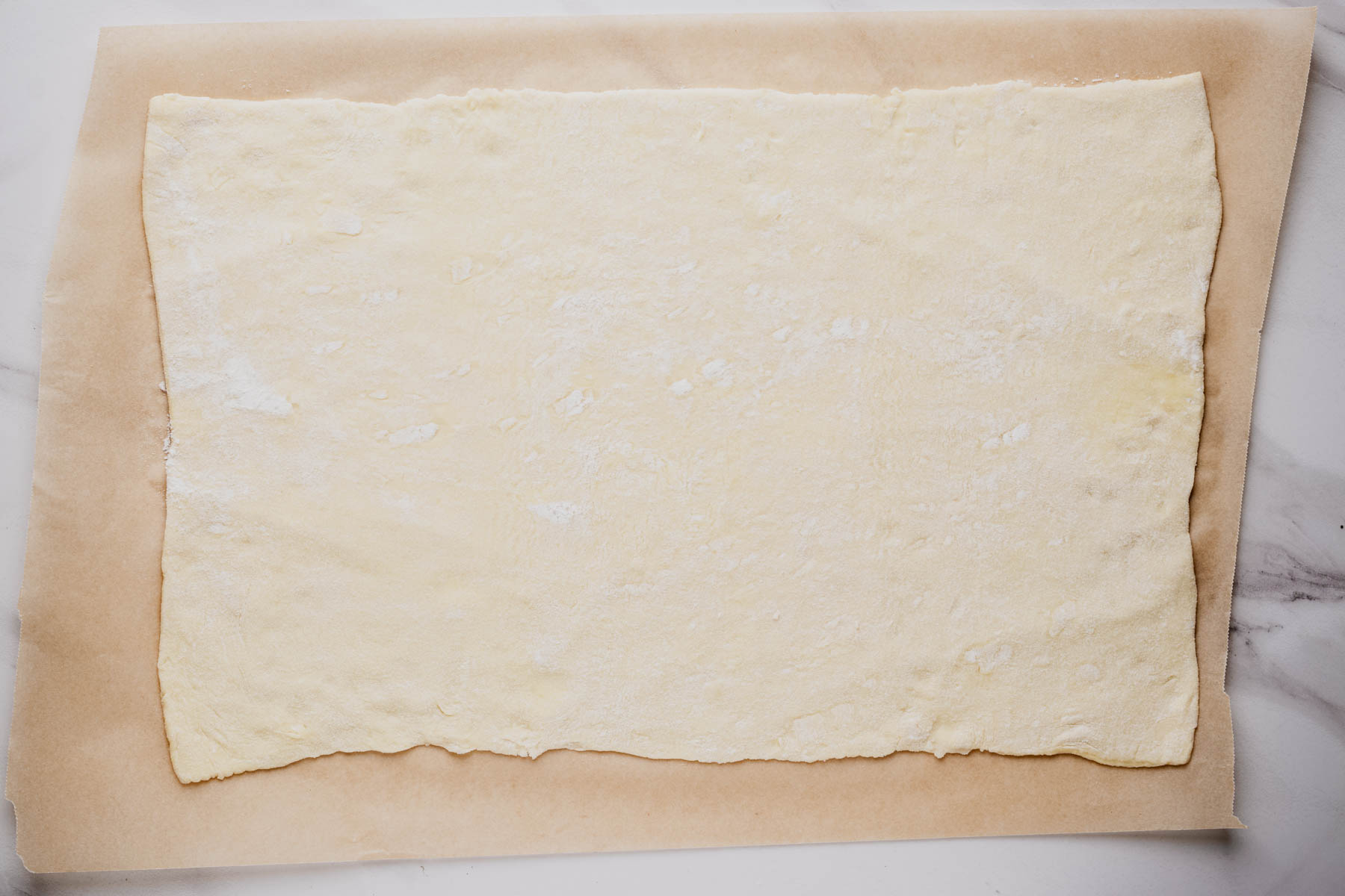 A sheet of puff pastry rolled into a rectangle on a lightly floured sheet of parchment paper.