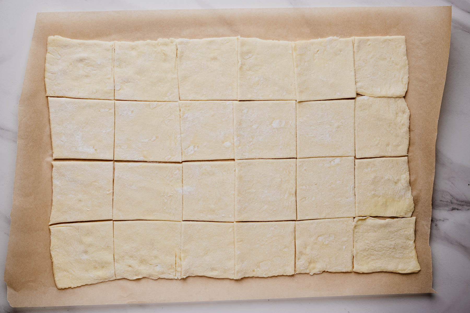 Rolled puff pastry cut into 24 equal squares on parchment paper.