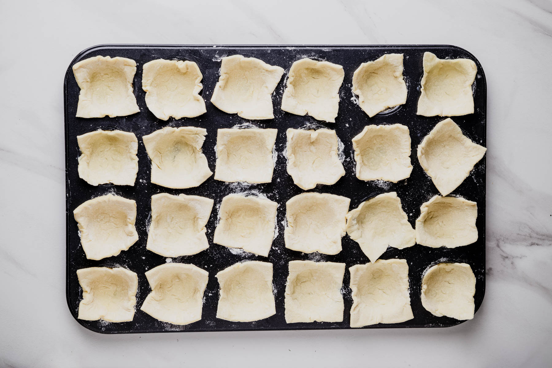 Puff pastry squares pressed into the wells of a buttered 24-cup mini muffin pan.
