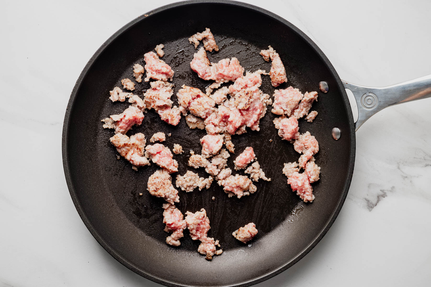 Mild Italian sausage cooking in crumbles in a black skillet.