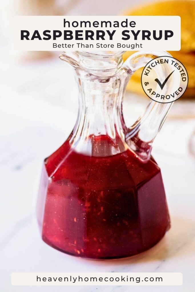 A glass syrup bottle filled with deep ruby-red homemade raspberry syrup sits on a light countertop with a softly blurred breakfast scene in the background. The Pinterest pin includes the text "Homemade Raspberry Syrup – Better Than Store Bought." This vertical Pinterest pin features a homemade raspberry syrup recipe from Heavenly Home Cooking.