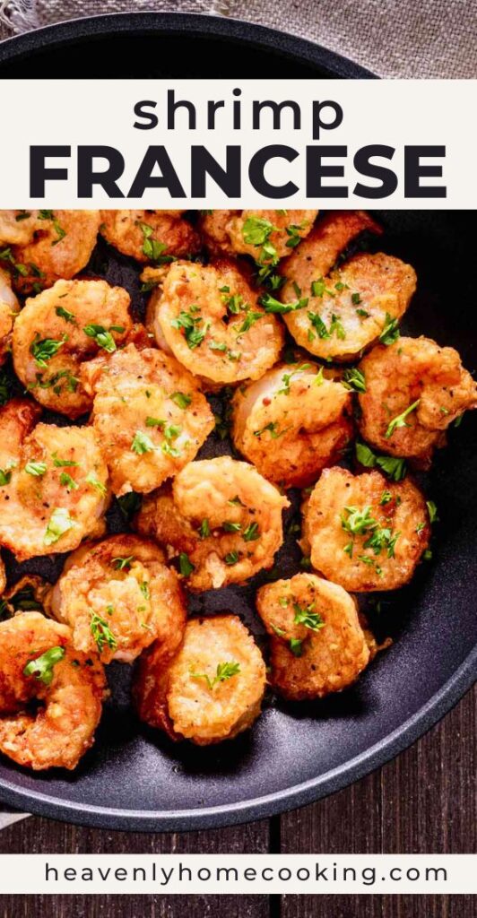 A skillet is filled with golden pan-fried shrimp Francese garnished with chopped fresh parsley, showcasing the lightly crisp coating on each shrimp. The Pinterest pin includes the text "Shrimp Francese." This vertical Pinterest pin features a homemade shrimp Francese recipe from Heavenly Home Cooking.