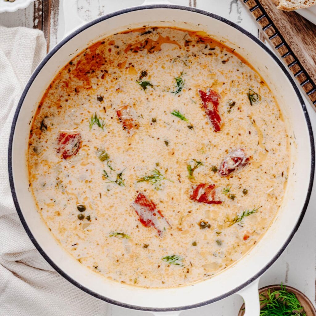 Overhead view of creamy smoked salmon chowder with salmon pieces, capers, and fresh dill in a white Dutch oven.