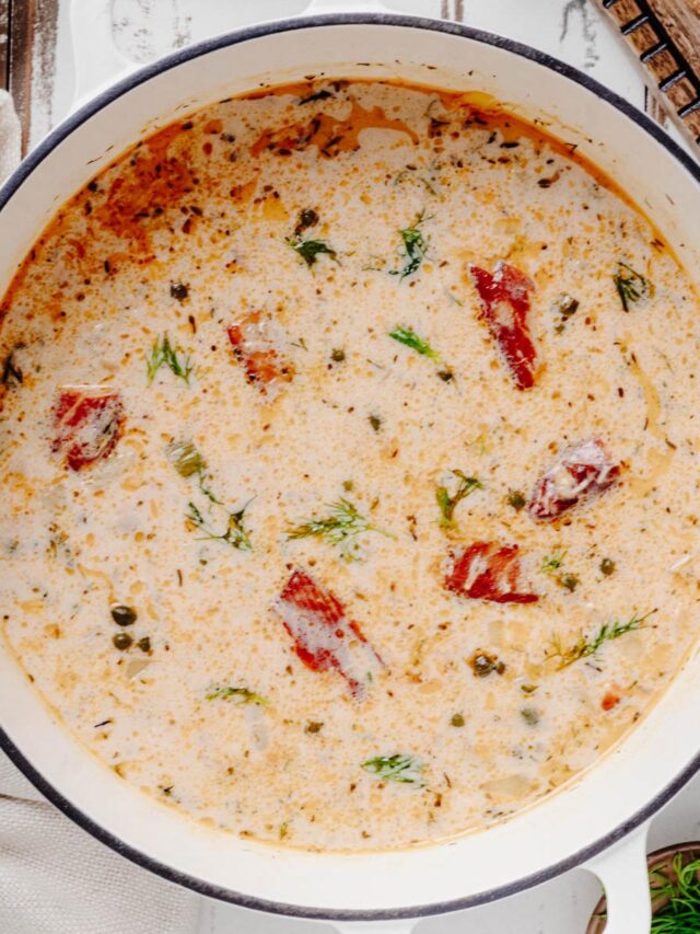 Overhead view of creamy smoked salmon chowder with salmon pieces, capers, and fresh dill in a white Dutch oven.