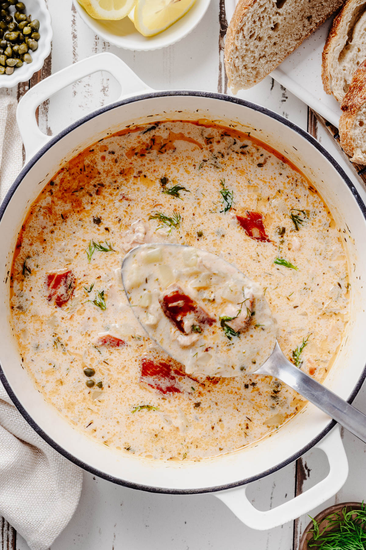 Ladleful of creamy smoked salmon chowder with tender potatoes, salmon, capers, and fresh dill above a Dutch oven.