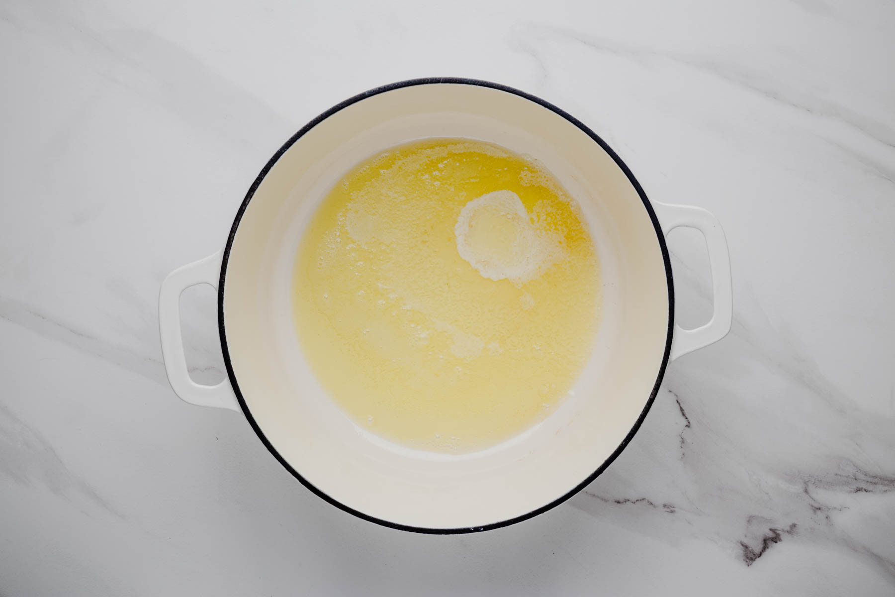 Unsalted butter and olive oil melting together in a white Dutch oven for smoked salmon chowder.