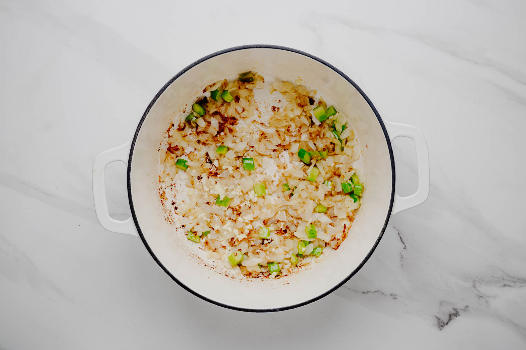Sautéed onion, celery, and minced garlic in a white Dutch oven for smoked salmon chowder.