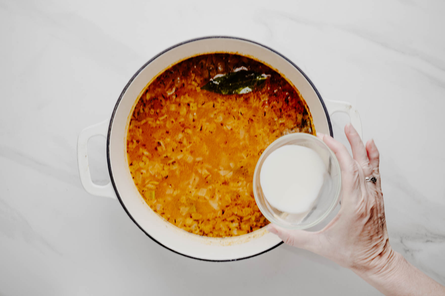 Cornstarch slurry being added to the seasoned potato chowder in a white Dutch oven.