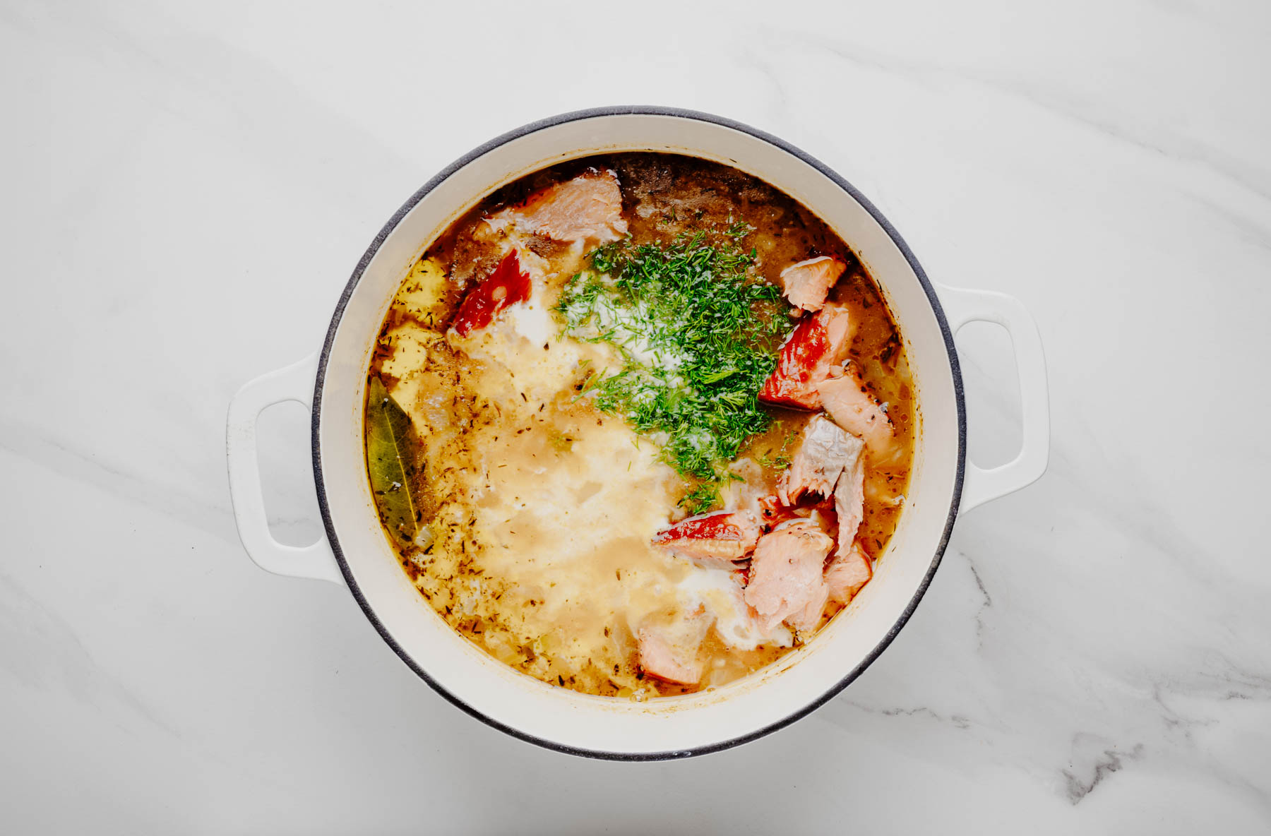 Hot-smoked salmon, half-and-half, and fresh dill added to potato chowder in a white Dutch oven.