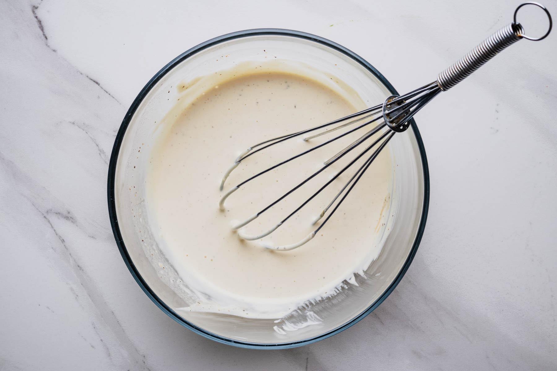 Creamy steakhouse dressing whisked until smooth in a glass mixing bowl. Process photo for a homemade Steakhouse Salad recipe from Heavenly Home Cooking.
