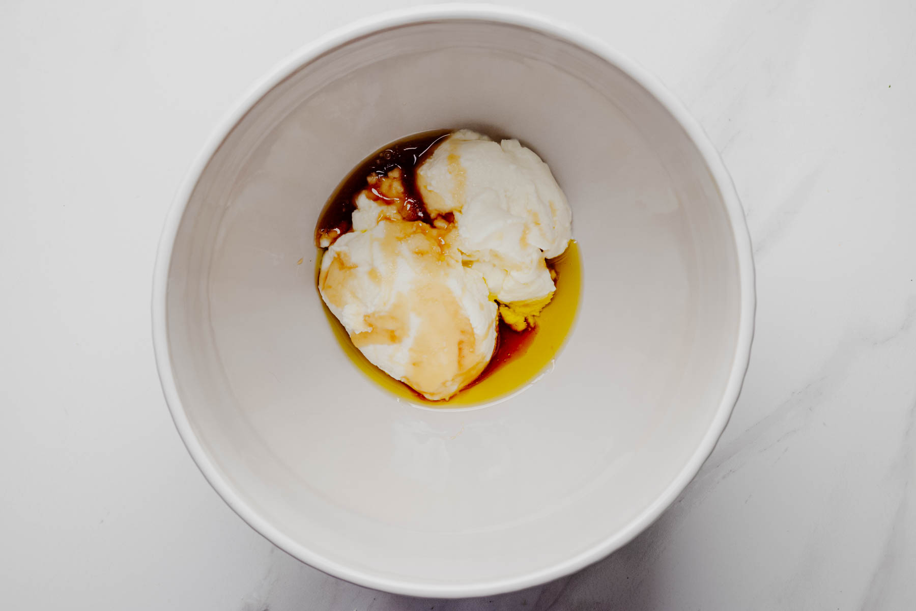 Ricotta cheese, honey, olive oil, and vanilla extract in a white mixing bowl before being stirred together.