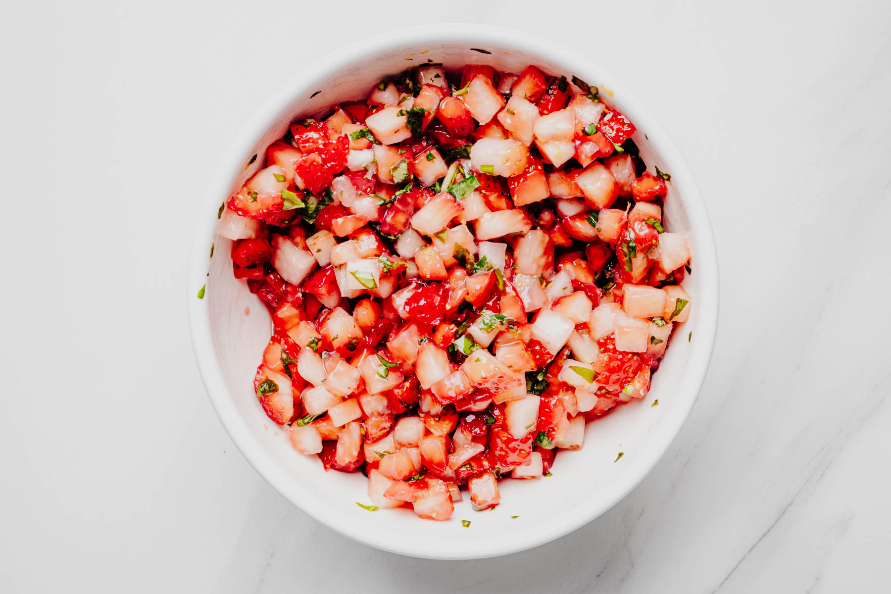 Fresh strawberry basil topping mixed together in a white bowl.