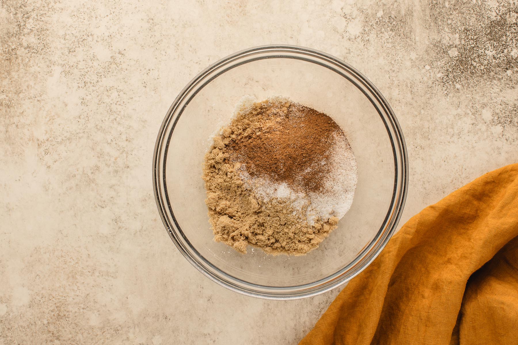Brown sugar, granulated sugar, cinnamon, salt, and flour in a glass bowl for apple muffin streusel topping.