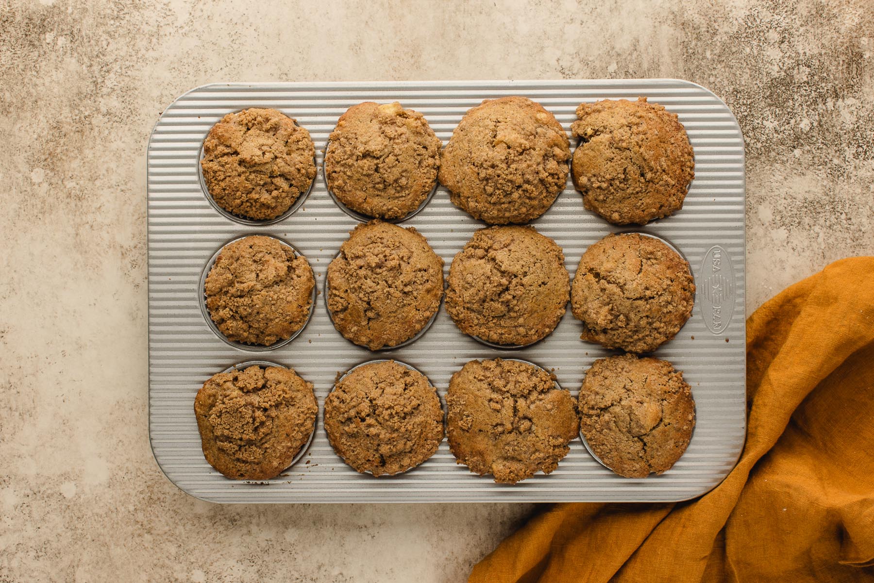 Freshly baked apple streusel muffins with tall golden brown tops in a muffin pan.