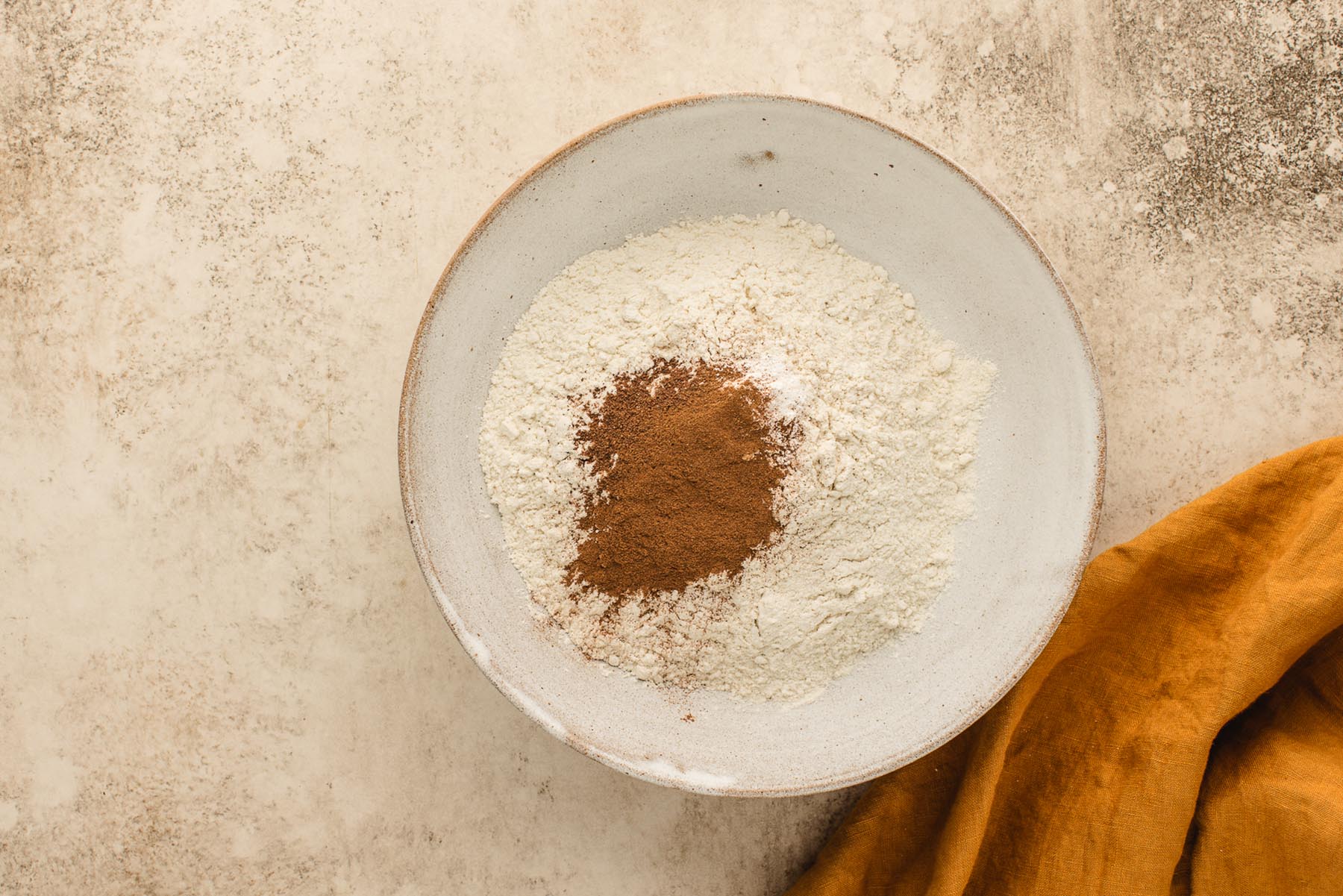 Flour, cinnamon, nutmeg, baking powder, baking soda, and salt in a bowl for apple muffin batter.