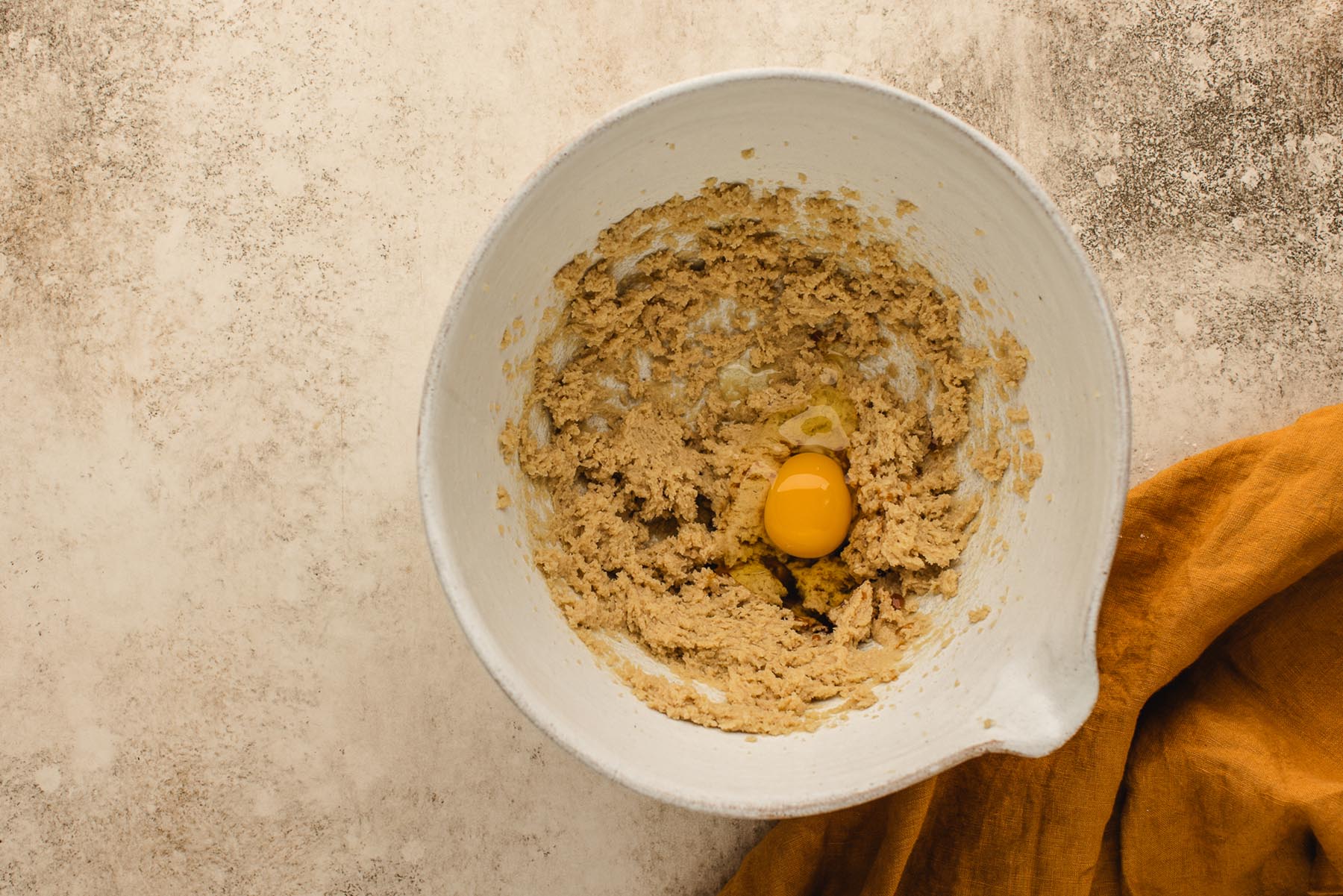 Egg and vanilla added to creamed butter and sugar mixture in a white mixing bowl.
