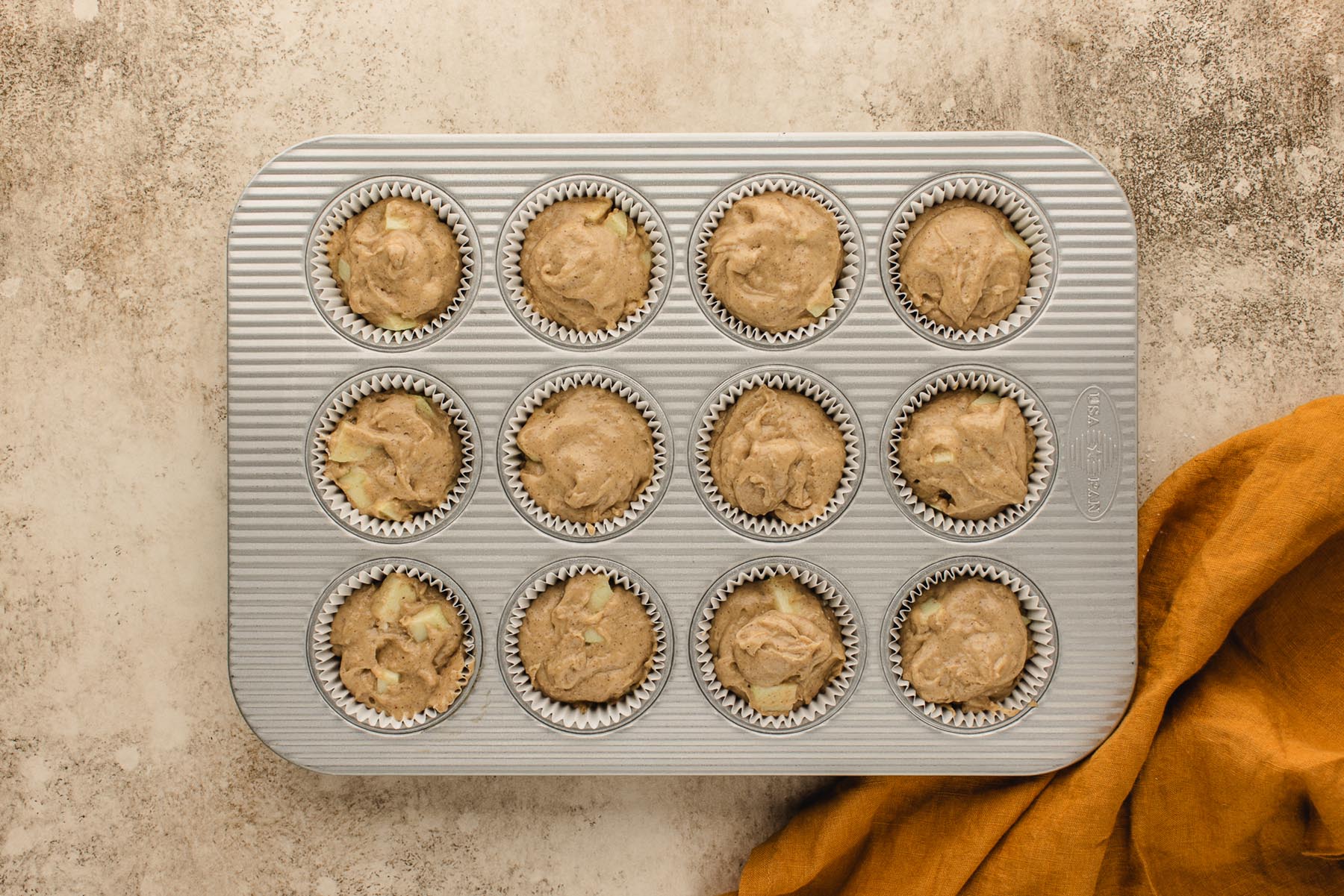 Twelve paper-lined muffin cups filled nearly to the top with apple cinnamon muffin batter.
