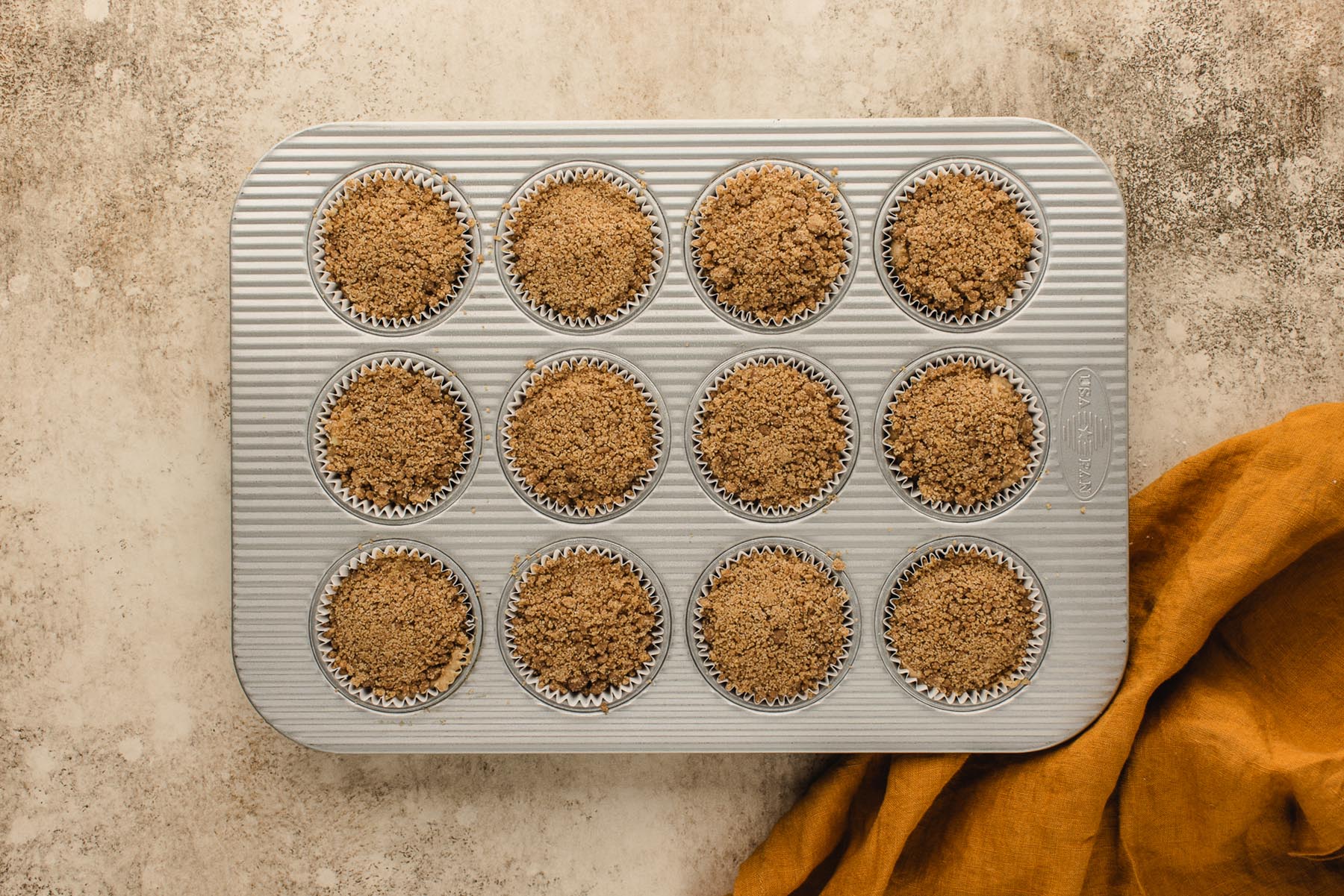 Unbaked apple muffins generously covered with cinnamon brown sugar streusel in a muffin pan.
